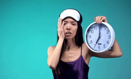 žena vyčerpaná špatným spánkem, držící budík v ruce.