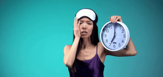žena vyčerpaná špatným spánkem, držící budík v ruce.