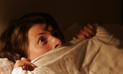 Vyděšená žena v posteli po nočním děsu.