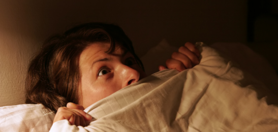 Vyděšená žena v posteli po nočním děsu.