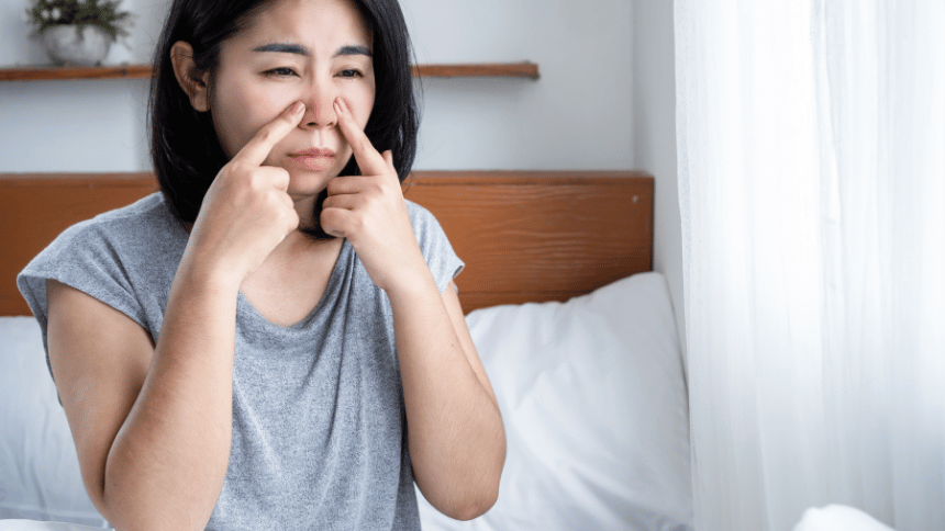 Žena sedící na posteli a držící se za bolavý nos.