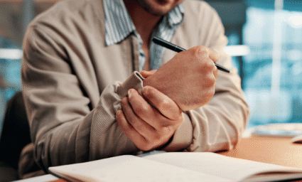 Muž drží si zápěstí a píše.