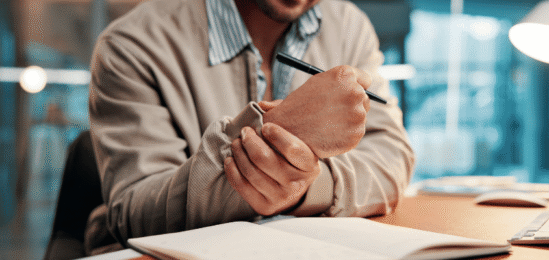 Muž drží si zápěstí a píše.